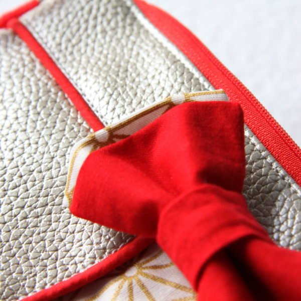 Pochette de soirée Ninie, en simili cuir or et passepoil rouge, détail du nœud rouge