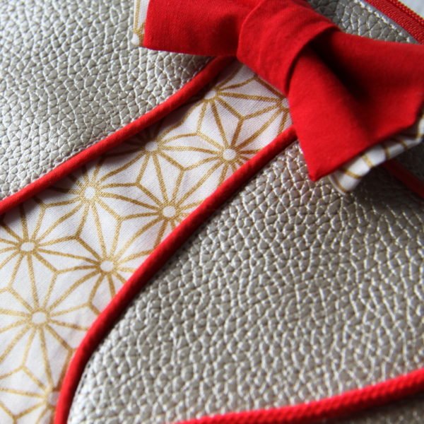 Pochette de soirée Ninie, en simili cuir or et passepoil rouge, détail du nœud